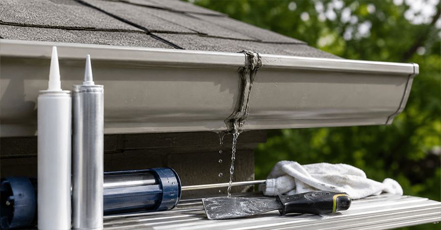 Gutter sealant tubes and caulking tools next to a leaking vinyl roof gutter joint.