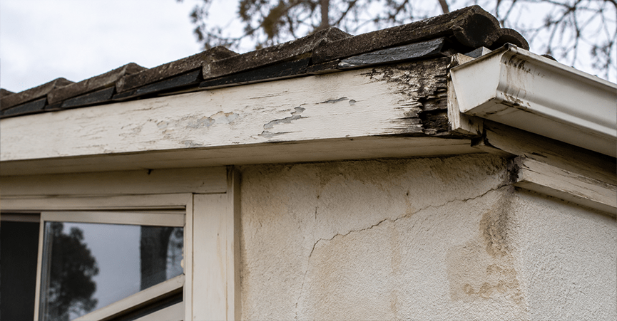 Water-damaged rotting fascia board and cracked exterior wall under a roofline.