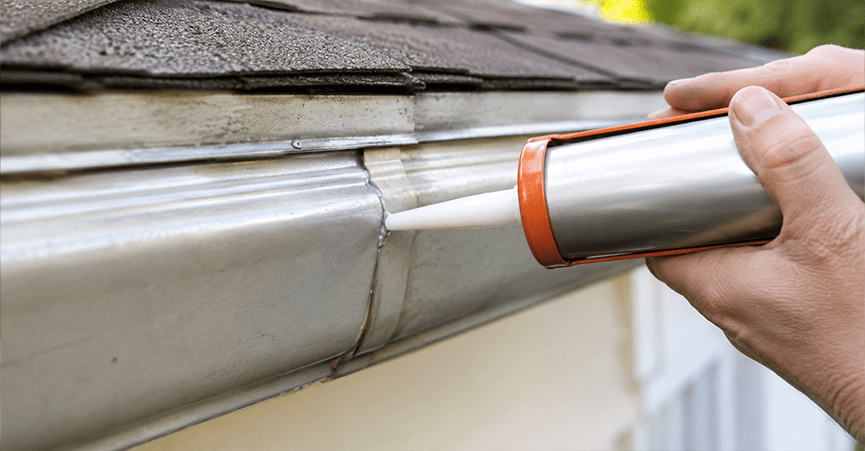 Applying waterproof sealant to a metal roof gutter seam using a caulking gun.